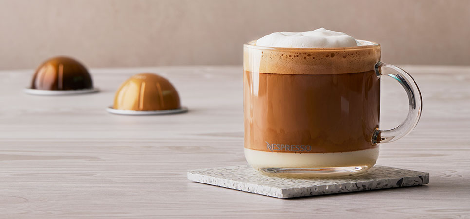 Un Cappuccino NESCAFÉ® Dolce Gusto® con cápsulas en el fondo 